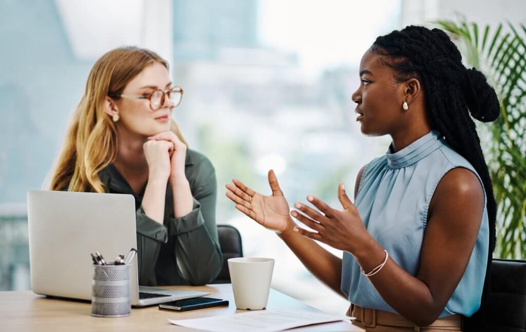 Two diverse businesswomen having a discussion to share ideas and plans while working together in an office.