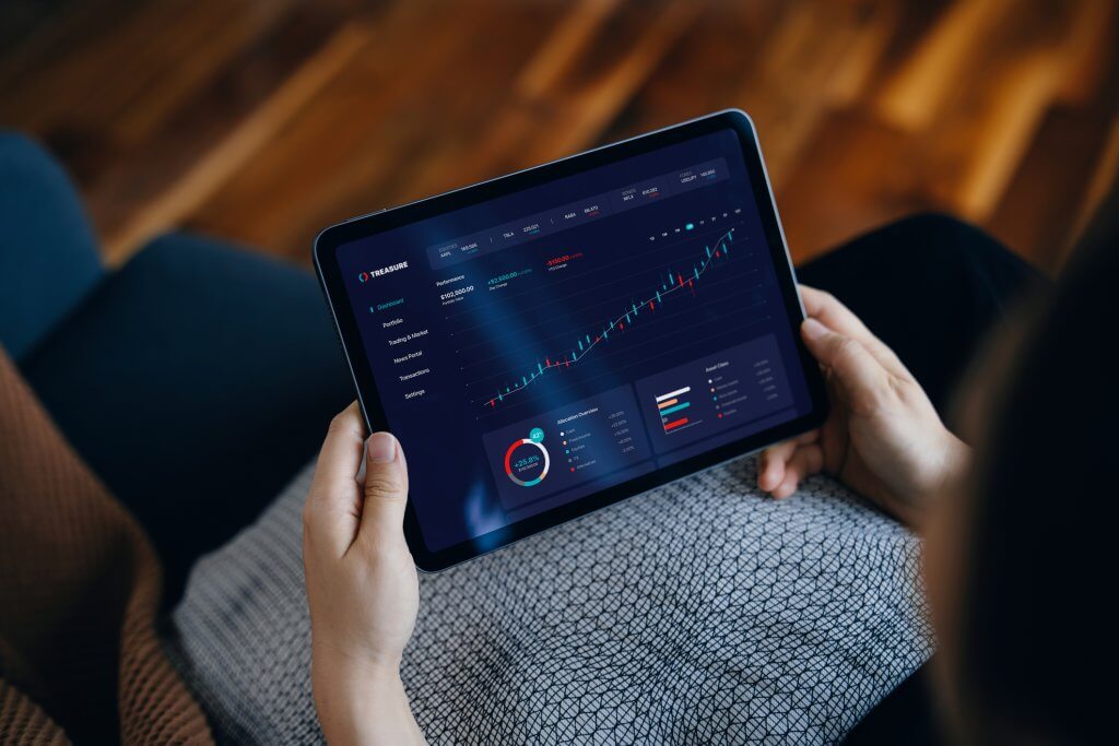 Over the shoulder view of young Asian woman managing finance and investment, analyzing stock market data on digital tablet at home. Stock exchange, banking, finance, investment, financial trading concept. Smart banking with technology
