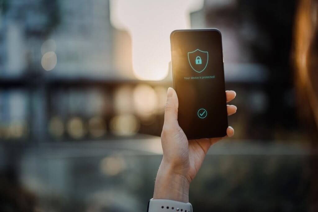 Close up of young woman using smartphone in downtown district in the city against urban city scene, with a security key lock icon on the smartphone screen. Privacy protection, internet and mobile security concept