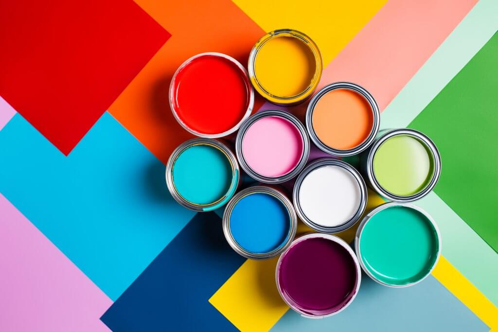 Top view of open cans with bright multicolored paints arranged on colorful geometric background representing concept of home repair and renovation supplies