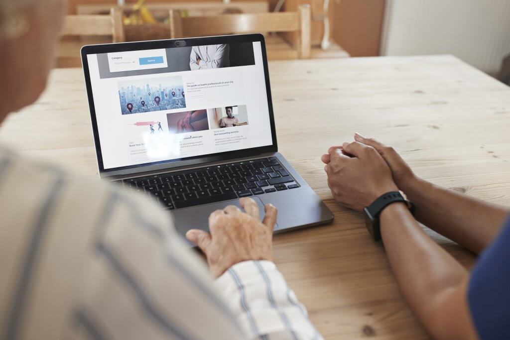 Cropped image of senior woman learning to book online appointment through laptop from caregiver at table