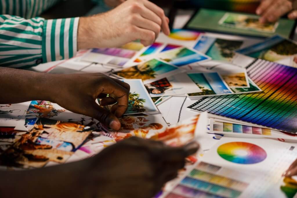 Close up shot of unrecognizable group of design professionals sitting in a meeting, sorting out various color swatches and photographs, making a new portfolio.