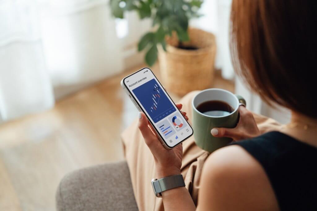 Over the shoulder view of young woman making financial plan and analysis via smartphone while taking a coffee break. Financial wellbeing concept.