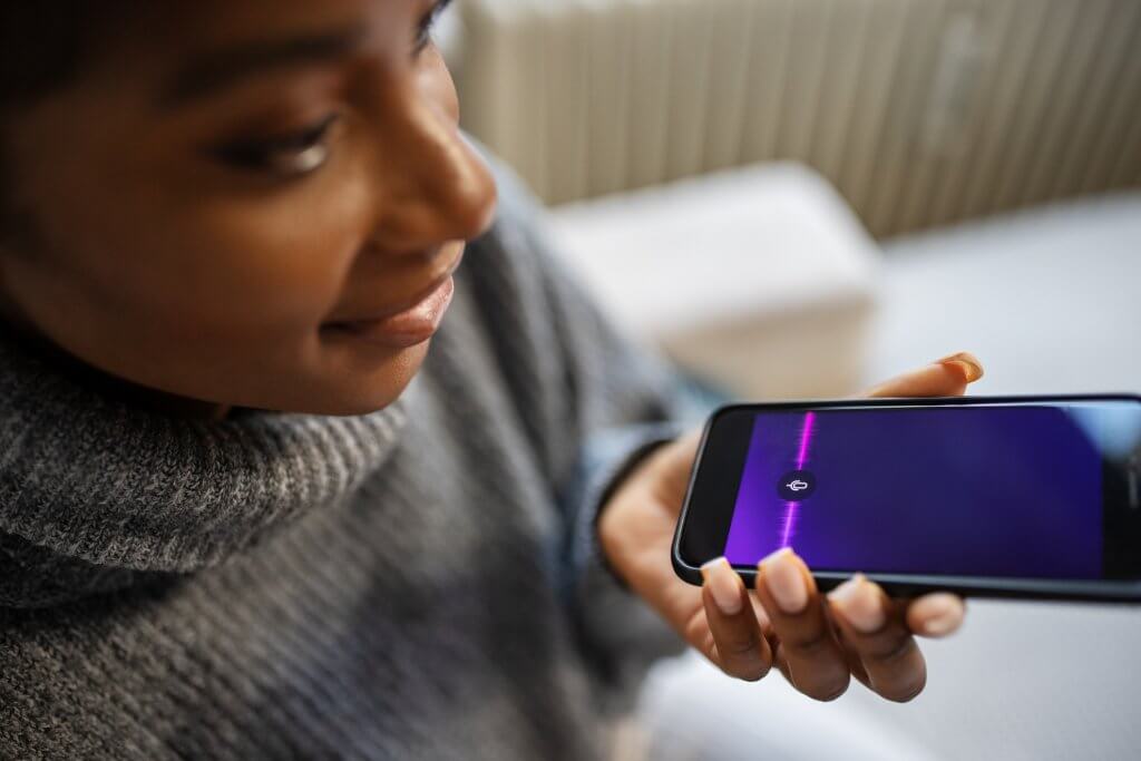 Close-up of young woman talk with virtual digital voice recognition assistant. African female using voice assistant on smartphone.