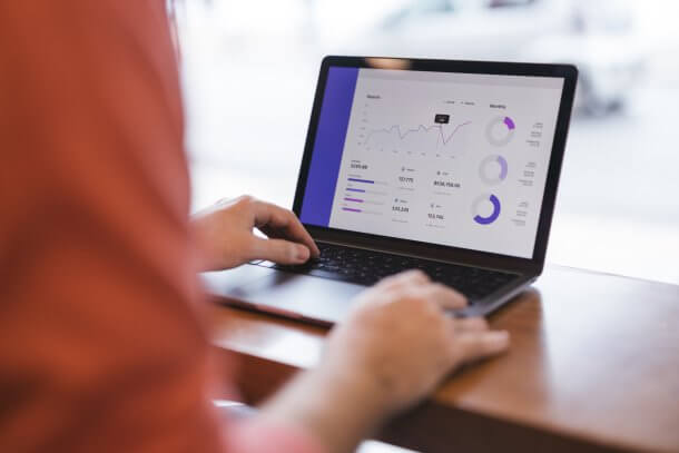 An individual is using a laptop to interpret statistical graphs and circular diagrams, showcasing data analysis in a work environment. The scene conveys professionalism, technology, and modern business tools.