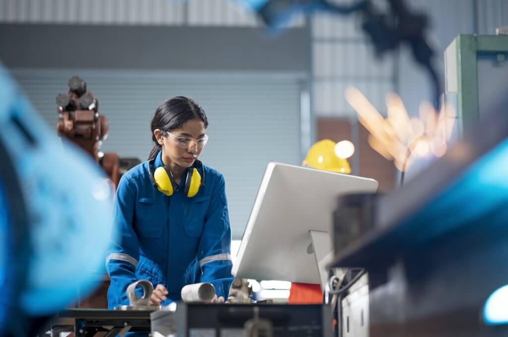 Female Industrial engineer working on desktop computer in robotic welding testing area of research and development in automobile industry. Productivity improvement concepts.