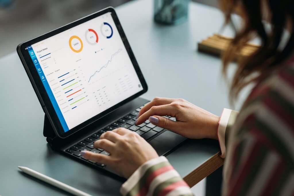 Woman in striped shirt working on tablet displaying colorful graphs and data analysis in a business environment.