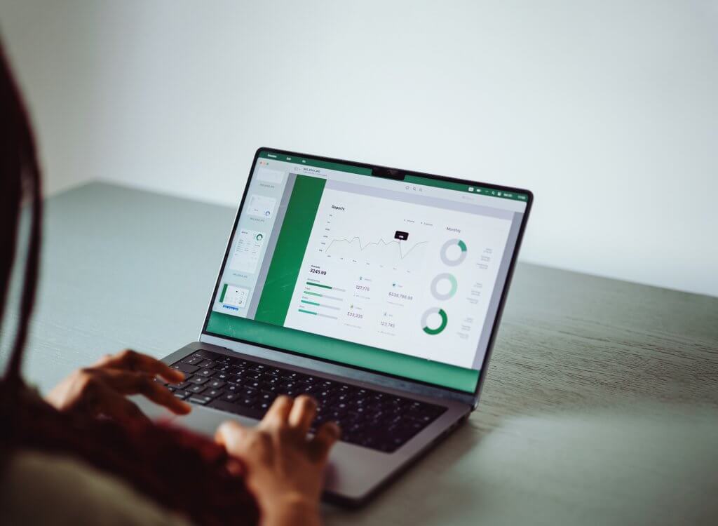 A business analyst working on a laptop, examining financial graphs and data visualizations for business and finance analysis.